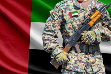 Fototapeta premium United Arab Emirates flag with soldier in military uniform holding assault rifle in front of it