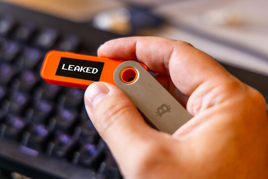hardware Bitcoin wallet held in white hand with Leaked message on screen