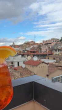 Close-up cropped vertical shot of unrecognizable woman stirring aperol spritz cocktail with straw sitting outdoors cafe on summer sunny day. Delicious alcoholic drink with citrus fruits in street bar.