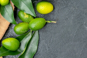 Fresh Green Kumquats with Natural Leaves on Dark Textured Background with Copy Space
