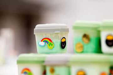 Clear plastic containers filled with green and colorful slime decorated with St. Patrick's Day themed stickers including rainbows and gold coins on shelf. Shows festive craft activity or party favor.