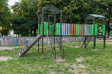 A modern outdoor playground with climbing ramps and platforms stands in a green park, designed for children's active play and physical development.
