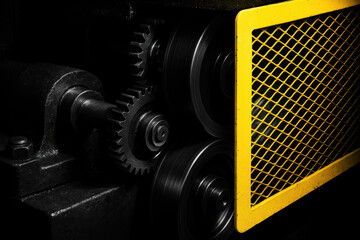Close up of an industrial machine with rotating metal gear parts. bright yellow safety guard highlights powerful, dark machinery, emphasizing precision and hazard prevention