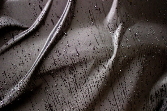 Wrinkles on wet black parachute fabric from rain highlight the shiny and contrasting texture of the waterproof material.