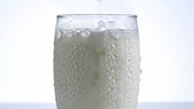 Chilled buttermilk-style Lassi drink with heavy condensation covering the cold exterior of the glass against a bright, isolated white setting appetizer, coolingeffect, beverage