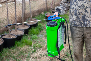 A gardener in protective clothing holds a bright green backpack sprayer, preparing to treat young plants in a nursery