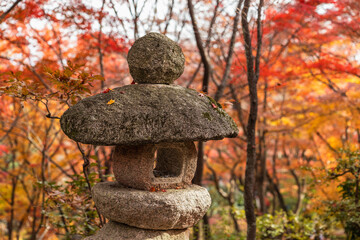 A traditional Japanese stone lantern (toro) stands majestically amidst a breathtaking autumn landscape, with vibrant red and orange maple leaves creating a stunning seasonal backdrop in a serene