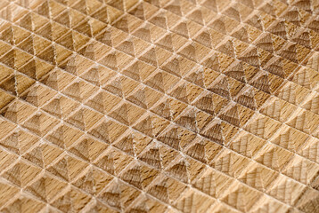The jagged surface of a flat wooden massager, many small rectangular pyramids, the natural texture and color of the wood