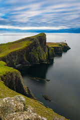 Vertical view of Neist Point cliffs and lighthouse on the Isle of Skye, Scotland, calm ocean and dramatic coastline under cloudy sky, iconic travel landscape with copy space.