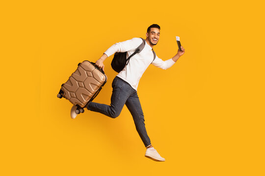 Portrait Of Young Happy Arab Man Jumping With Suitcase And Pasport, Ready For Vacation Trip, Excited Middle Eastern Guy Running With Luggage Over Yellow Background, Full Length Shot, Copy Space