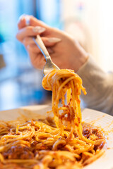 Close-up of a hand twirling spaghetti on a fork over a plate of tomato sauce. A delicious Italian pasta dish in a warm, cozy dining room.