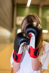 Close-up of a person wearing boxing gloves in a defensive stance inside a gym. Concept of training, strength, focus, and sports activity.