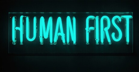Obraz premium Bright neon sign displays words Human First. Dark background emphasizes glowing turquoise lettering. Simple, direct message.