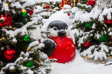 Cute red breasted bird figure in snow among decorated Christmas trees with baubles and lights, Moscow, Russia.