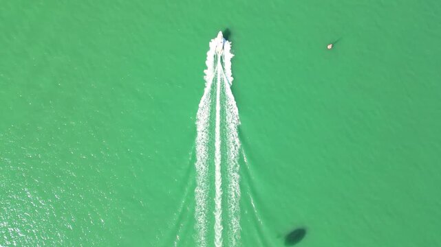 Top down parasailing boat wake on emerald sea. 4K horizontal drone footage shows a speedboat cutting vivid green water near Batumi, Georgia, with white foam trails and visible parachute shadow.