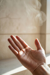 Hand with fingers extended, palm facing up, with steam rising in soft light against a textured background