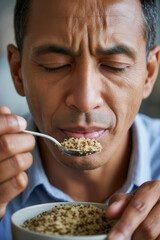 Man holds spoon with quinoa close to mouth, with bowl of quinoa in hands and shirt collar visible
