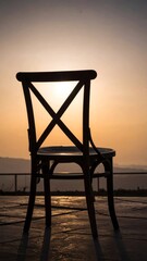 Silhouette of a wooden chair against a warm, golden sunset backdrop, creating a peaceful scene.