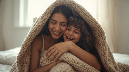 Mother and daughter sharing a warm hug under a cozy knitted blanket, laughing together
