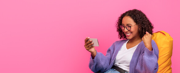 A woman is sitting on a yellow bean bag chair. She is looking at her phone and smiling. Her curly...