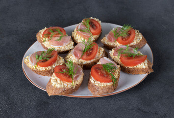 Bruschetta with bacon and tomatoes on rye bread toast on white plate on gray table