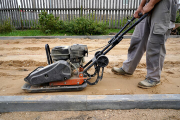 worker rams the ground with a vibrating machine.Side view.