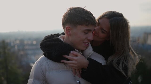 A young couple embraces affectionately with the Paris skyline in the background The woman hugs and kisses the man showcasing their love and connection Handheld shot.