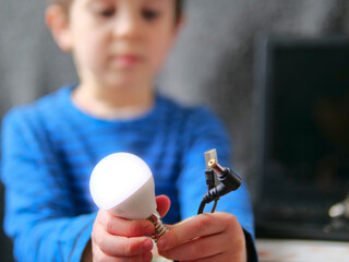 Boy Holding Glowing LED Lightbulb and Power Cables in STEM Concept - clean energy, smart solutions, science kits, innovation, startup, brilliant idea