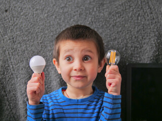 Excited Young Boy Holding Two Different Lightbulbs with Funny Surprised Expression - bright idea, innovation or future of energy copy space concept