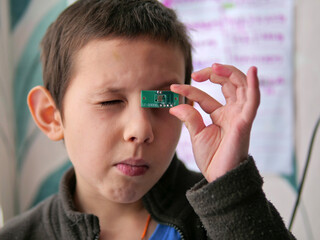 Boy Curiously Inspecting a Small Green Circuit Board Component - STEM Learning for Kids: A Child Examining an Electronic Part Close to His Eye