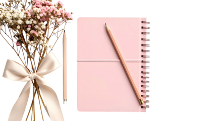 A pink notebook with a pencil and floral bouquet, tied with a ribbon, against a black backdrop