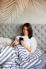 Woman lying in bed using smart phone after waking up in the morning