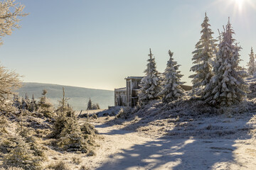 Zimowy krajobraz górski ze schroniskiem i ośnieżonymi świerkami w blasku słońca. Karkonosze,...