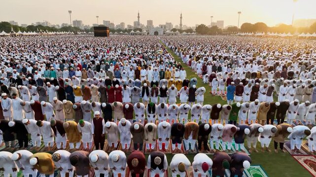 Spiritual wide-angle view of thousands of muslim worshippers bowing in ruku prayer on a vast open ground in india.