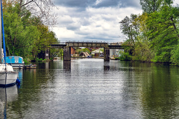 2025-05-06 A LOVELY CANAL WITH A BOAT AND NICE REFLECTION AND GREENERY ON THE BANKS AND A METAL CROSSING BRIDGE IN NORWICH ENGLAND