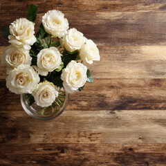bouquet of white roses in a clear glass vase sits elegantly on a textured wooden table, creating a warm and natural still-life scene