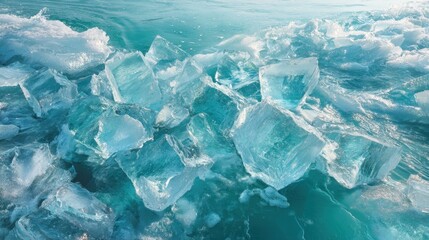 Ice chunks in various sizes float on tranquil waters under sunlight. The clear blue of the ice contrasts beautifully with the turquoise water, creating a serene scene.