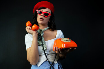 A woman in a red hat and sunglasses is holding an antique telephone.