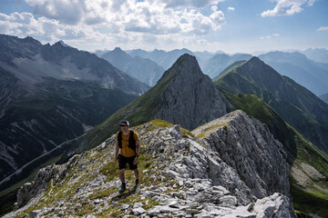 Fototapeta premium Mountaineer standing on a rocky ridge with breathtaking panoramic view over countless peaks in Tyrol, Austria, dramatic alpine landscape and clear sky.