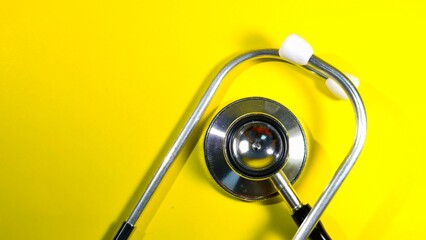 A top-down view of a classic chrome stethoscope centered on a bright yellow surface, representing...