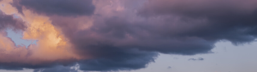 Naklejka premium dramatic sunset sky panorama: contrast of dark storm clouds and bright orange glow at twilight