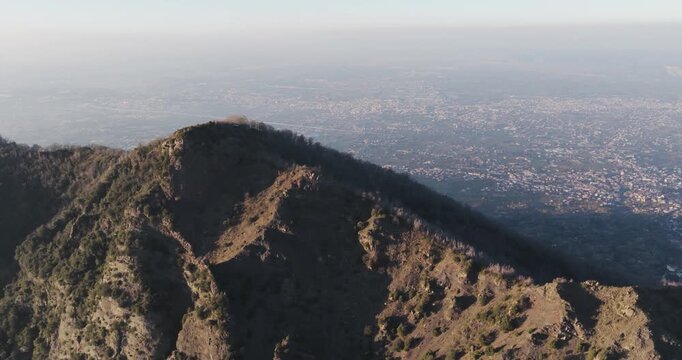 Aerial view of Mount Vesuvius, showcasing its rugged terrain contrasting with the distant cityscape, Ercolano, Campania, Italy.