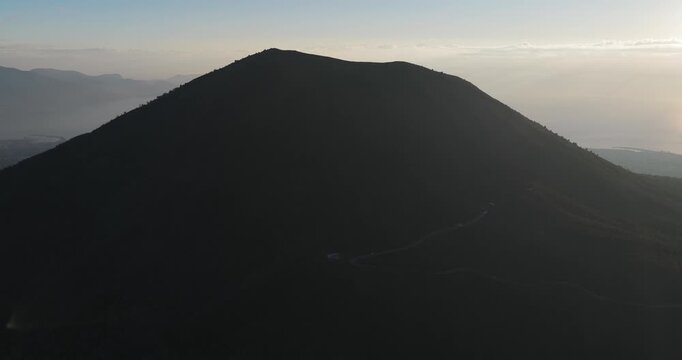 Aerial view of Mount Vesuvius, a dark, imposing silhouette against the fading light of dusk, casting long shadows over the landscape, Ercolano, Campania, Italy.