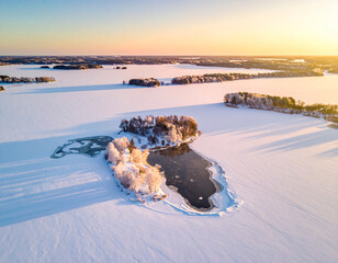 Stunning Aerial View of a Frozen Lake with Snow-Covered Islands at Sunrise, Golden Hour Light Over Frosty Winter Landscape and Icy Wilderness