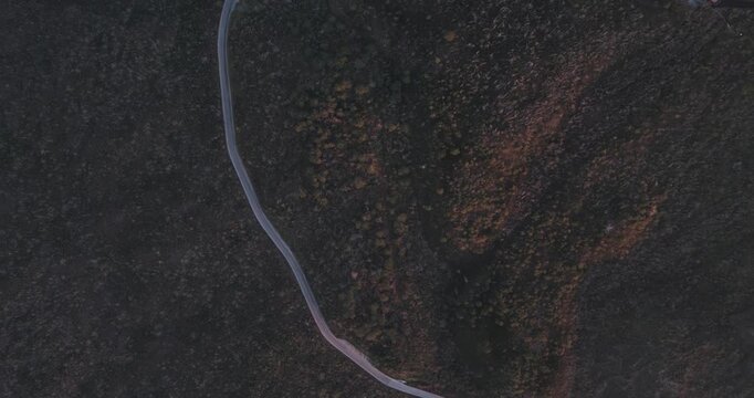 Aerial view of Vesuvio road winding through rugged terrain, a lone car ascends amidst the shadows and hints of sunset, Ercolano, Campania, Italy.
