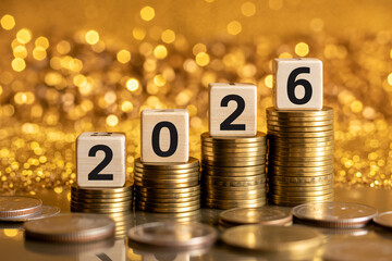 Stacks of coins with 2026 on wooden blocks in golden lighting on bokeh background for financial growth