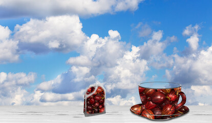 Against the background of the blue sky is a cup and saucer and a tea bag with gooseberries.