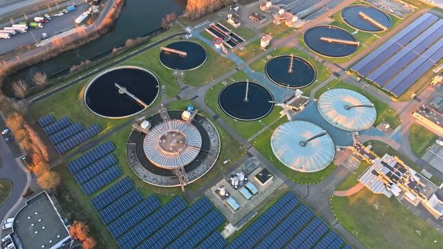 Top-down aerial view of modern wastewater treatment facility featuring circular settling tanks and large solar panel fields, showcasing water management and sustainable infrastructure