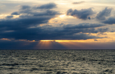 Dramatic seascape with sun rays breaking through dark storm clouds over the ocean