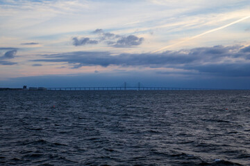 Fototapeta premium Wide seascape view of the Oresund Bridge on the horizon under a cloudy evening sky with a vapor trail